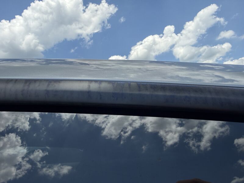Hazy chemical film with a faint blue tint on Tesla window trim, visible in direct sunlight