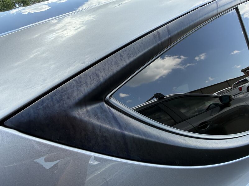 Mottled purple-and-blue chemical staining on the black trim around a Tesla Model Y rear quarter window