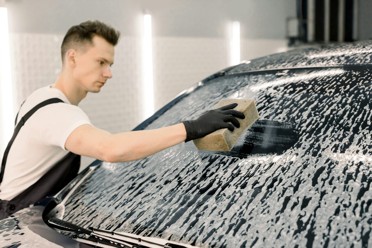 A professional detailer cleaning a vehicle windshield with a microfiber towel
