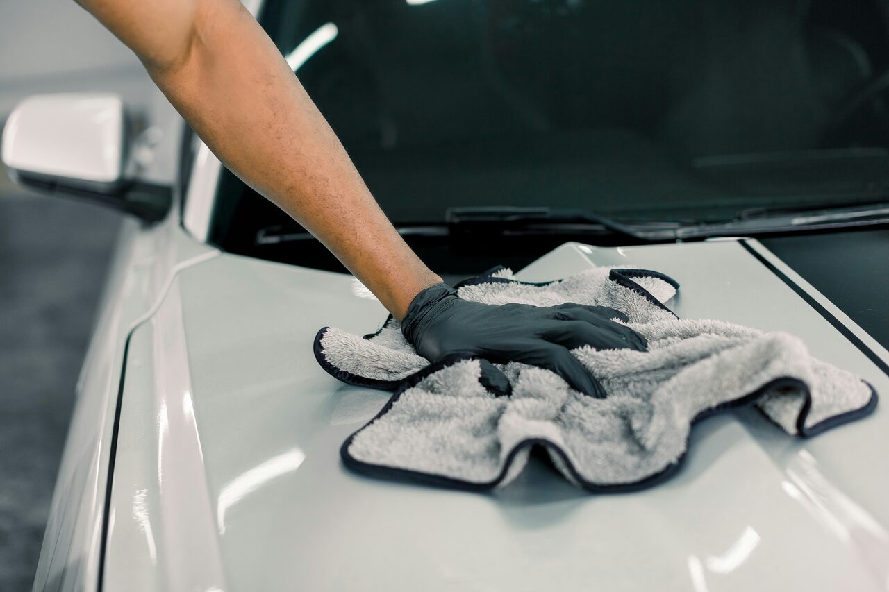 A detailer wiping down a freshly washed car panel with a microfiber towel