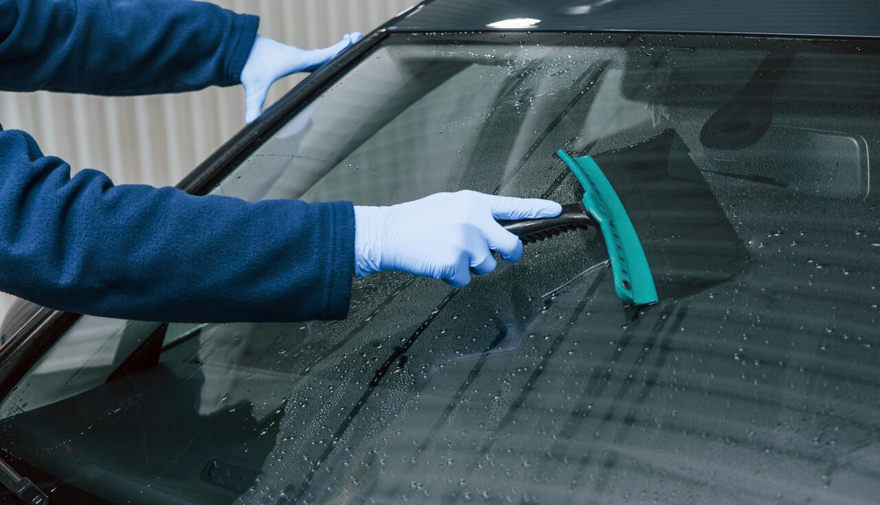 A detailer using a squeegee to clear water from a windshield — controlling wash-water runoff is required under Charlotte's stormwater ordinance
