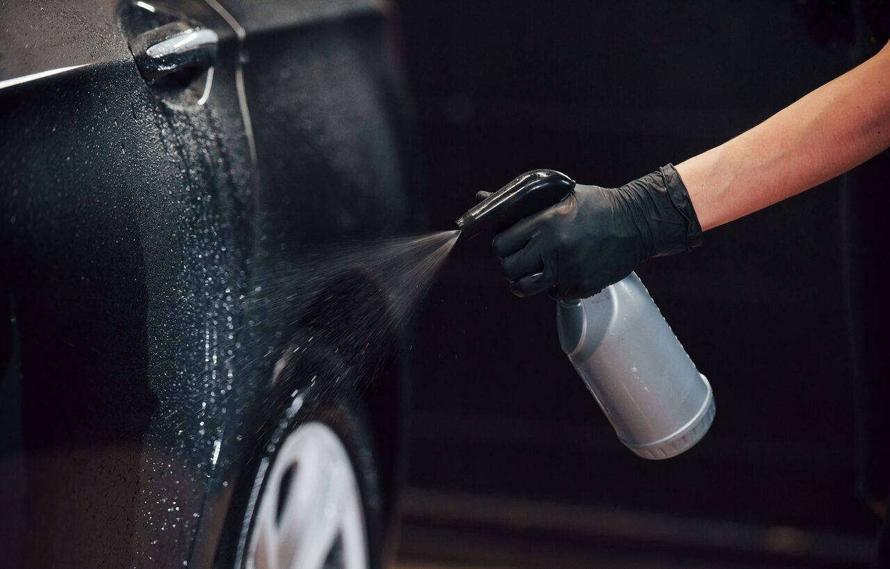 A mobile detailer applying a rinseless spray detailer to a glossy black car panel